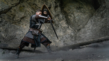 A medieval warrior stands poised with sword and shield amidst a rocky landscape. © horimono