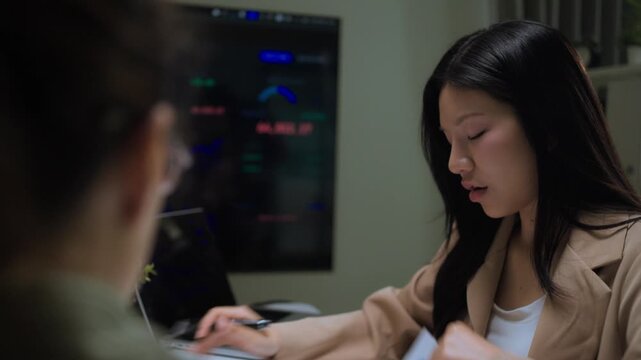 Close Up of Two Asian Women in Side Profile Having a Business Conversation. Professional Interaction and Workplace Communication Detail.