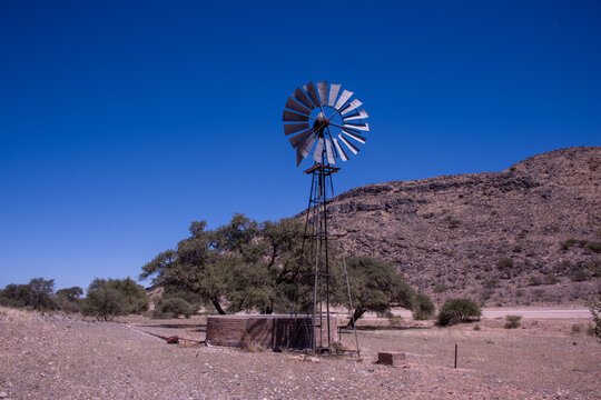 A wind-powered well stands in the Namibian desert, its steady rotation drawing hidden groundwater to the surface, turning wind into life across an arid, sunlit landscape.