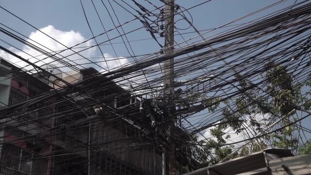 Messy power wires are tangled on the electrical pole, creating a chaotic arrangement of internet cables and powerlines in Thailand.