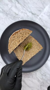 Spreading vibrant, herbaceous pesto on bread adds an instant, fresh Mediterranean flair. It transforms a simple slice of bread into a savory, aromatic snack or appetizer.