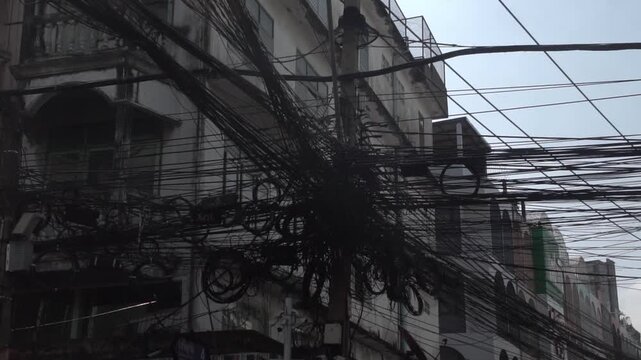 Messy power wires are tangled on the electrical pole, creating a chaotic arrangement of internet cables and powerlines in Thailand.