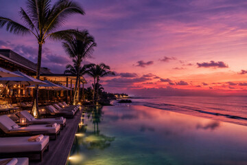 Luxury infinity pool at tropical beachfront resort during a dramatic purple and orange sunset sky