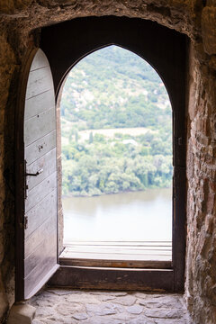 Old wooden door opening into nothingness in a historic castle on a mountaintop, with a river and forest landscape in the distance