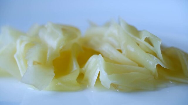 Pickled ginger gari, traditional japanese tsukemono condiment for sushi and sashimi, slowly moving on white plate, isolated on white background, revealing its texture. Pickled ginger gari on plate