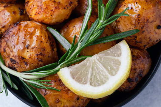 Close up freshly crispy roasted potatoes are placed in a bowl with a slice of lemon and sprigs of rosemary on top. Homemade comfort food and healthy side dishes. top view