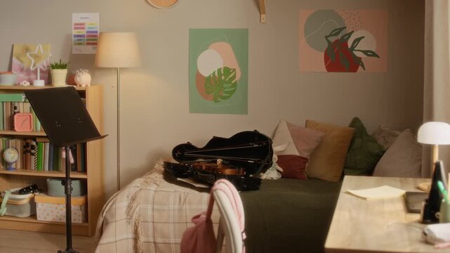 Establishing shot of violin lying in case on bed next to music stand in child bedroom. Setup serves as background for music education, online tutoring, or classical instrument school advertisement