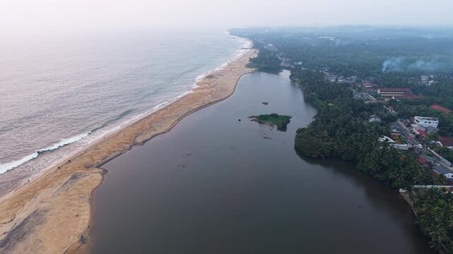 Aerial view of Mahamodara Lake separated from the ocean by a sandy beach strip with lush tropical greenery and buildings, Galle, Southern Province, Sri Lanka.