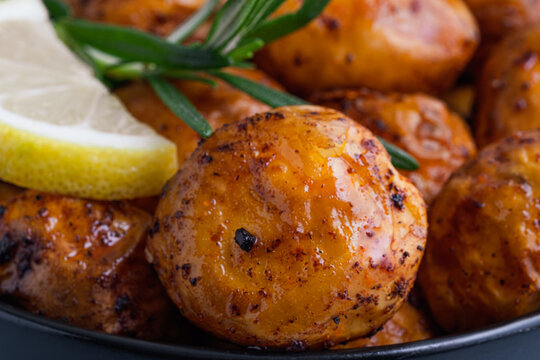 Close up freshly crispy roasted potatoes are placed in a bowl with a slice of lemon and sprigs of rosemary on top. Homemade comfort food and healthy side dishes