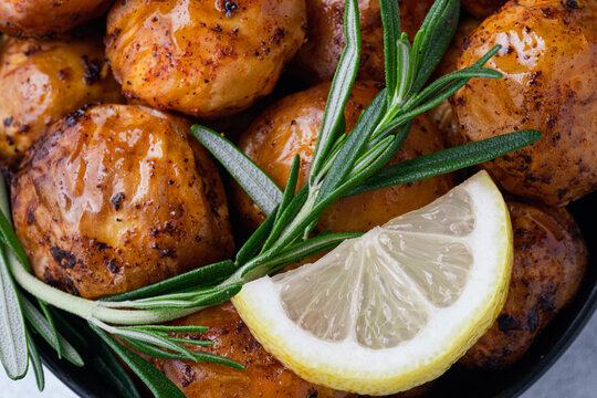 Close up freshly crispy roasted potatoes are placed in a bowl with a slice of lemon and sprigs of rosemary on top. Homemade comfort food and healthy side dishes