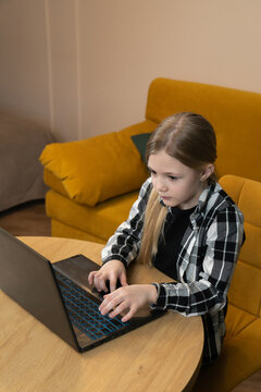 Little student focused on completing homework and preparing school projects, utilizing a laptop computer for distance learning and online education from a cozy home environment. Vertical photo