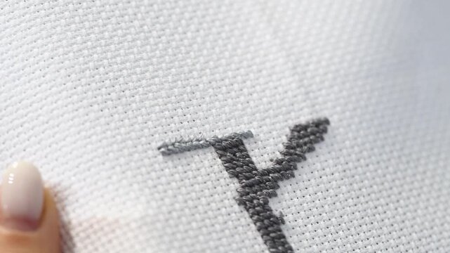 Close up detailed black cross stitch embroidery process on white fabric with focused needlework