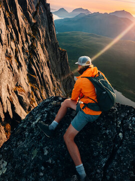 Brave man looking down from the mountain cliff edge travel solo in Norway climbing extreme summer vacation adventure trip outdoor, traveler with backpack enjoying views freedom and harmony with nature