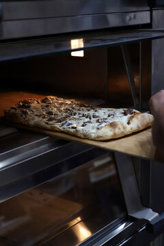 pizzero sacando del horno una pizza artesanal de carne y queso fundido