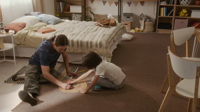 Asian man and multiethnic child sitting on floor, coloring cardboard target and celebrating with high five. Perfect for parenting, family bonding, and creative play marketing campaigns