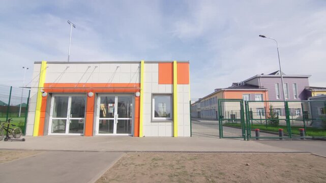 Entrance checkpoint building features colorful accents alongside glass double doors. Clean concrete pathway leading toward facility entrance