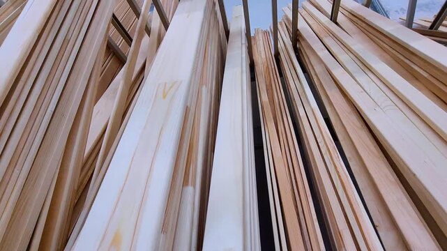 Wooden planks, boards, and moldings neatly stacked in rows on shelving racks inside a lumber warehouse or a large hardware store, ready for construction, renovation, or carpentry projects