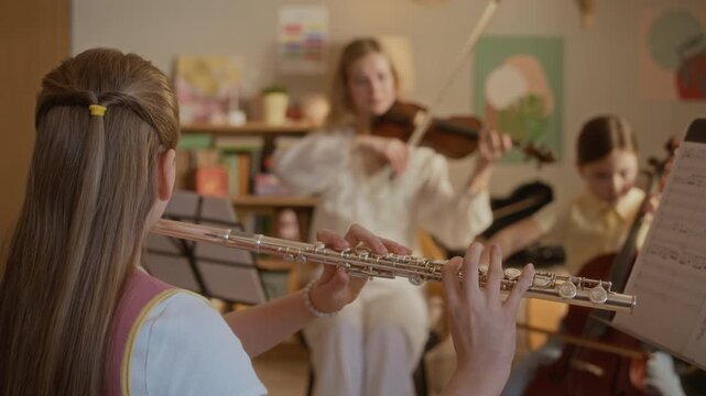 Handheld shot of children practicing flute and cello during music lesson with young female teacher playing violin. Video is ideal for promoting private music tutoring and arts education programs