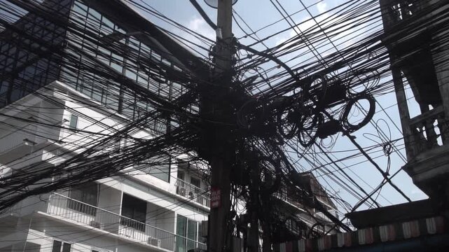 Messy power wires are tangled on the electrical pole, creating a chaotic arrangement of internet cables and powerlines in Thailand.