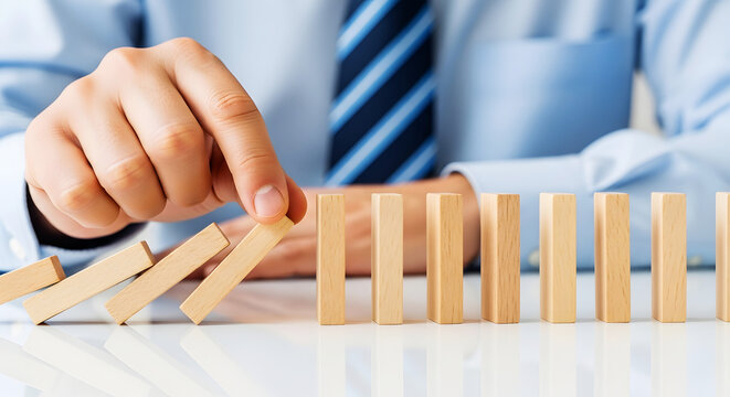 Man in blue shirt and tie nudging wooden dominoes in a row game hand