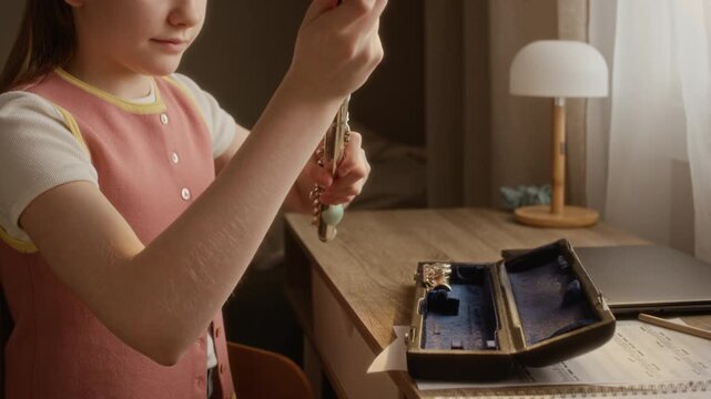 Handheld shot of Caucasian girl opening instrument case and assembling silver flute at desk. Video is perfect for marketing music schools, private tutoring, and childrens creative education