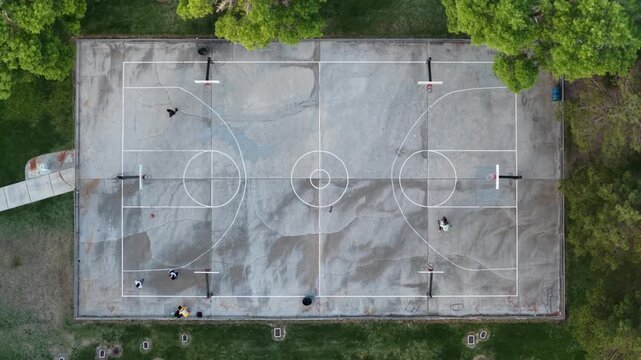 Aerial view of people playing on a concrete basketball court surrounded by lush green trees in Summerlin South, Nevada, United States.