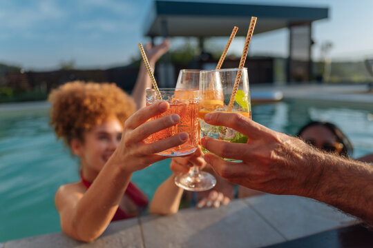 Friends clinking cocktail glasses in swimming pool