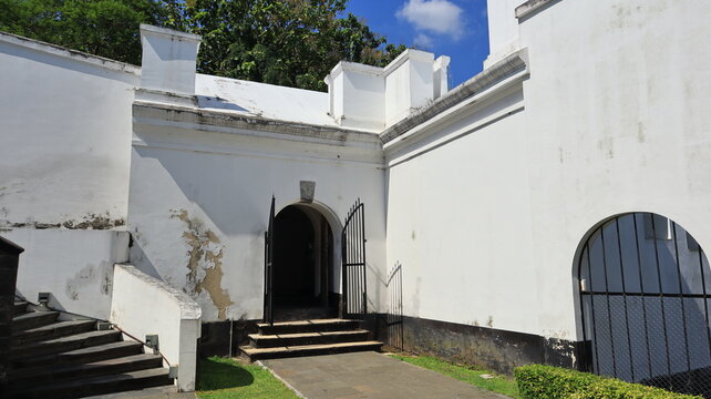 An arched doorway with a gate made of black iron bars is set into the boundary wall of an old building.