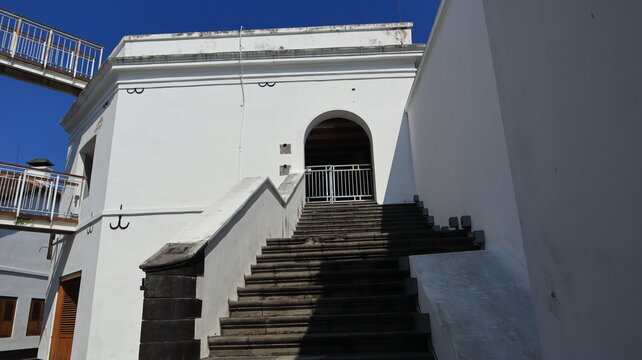 A beautiful stone staircase leads to the second floor of a white building attached to the boundary wall.