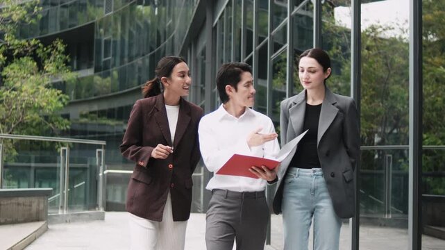 Three businesspeople, male Asian manager and female colleagues walking and discussing business report jobs, and investment at outdoor workplace office with high-rise building, and urban lifestyles.