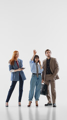 Obraz premium Trendy office group waving during phone call in white studio. Concept of office fashion, team greeting, personal branding, smart casual style, and social content.