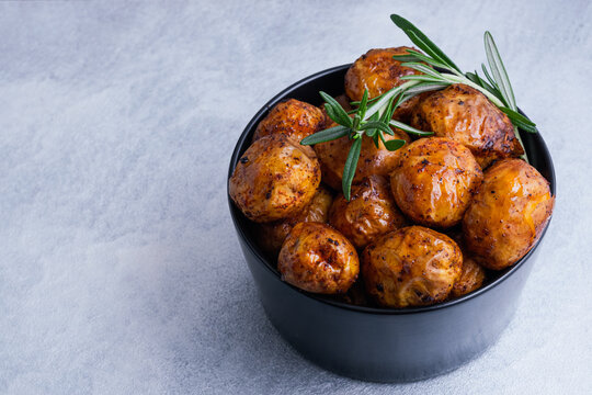 A close up food photograph of golden roasted baby potatoes served garnished with fresh rosemary sprigs on a blue background. Homemade comfort food and healthy side dishes. top view