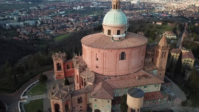 Aerial view of Santuario Madonna di San Luca with its historic green dome on a wooded hill overlooking the city skyline in Bologna, Emilia-Romagna, Italy.