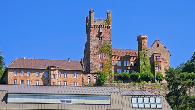 Historic castle tower and stone building in Neckarsteinach, Germany, rising above village rooftops with ivy-covered walls, blue sky and scenic medieval architecture in the Neckar Valley.