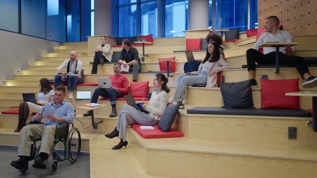 Group of people attend a business conference or educational lecture in a modern tiered amphitheater. Diverse colleagues are actively engaged, learning and collaborating in an innovative office space