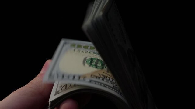Close-up of hand flipping through stack of U.S. hundred dollar bills in slow-motion