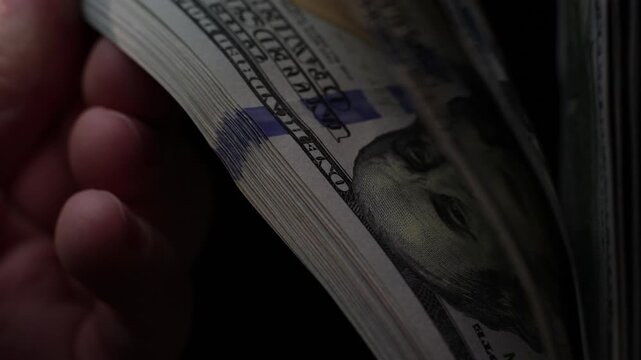 Close-up of hand flipping through stack of U.S. hundred dollar bills in slow-motion