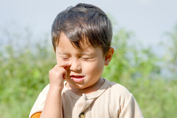 Fototapeta premium Portrait of a young boy with closed eyes touching his nose, outdoors in a natural setting