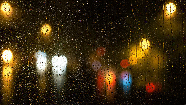 Raindrops on window glass with blurred city lights at night, creating moody urban atmosphere for cinematic or mood setting
