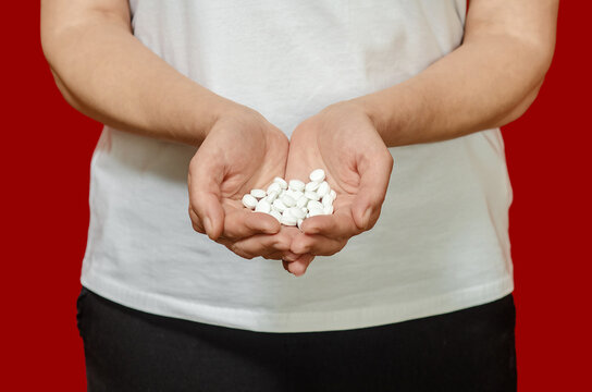 Rerson holding handful of pills on red. Risks of drug abuse, addiction and pharmaceutical dependence