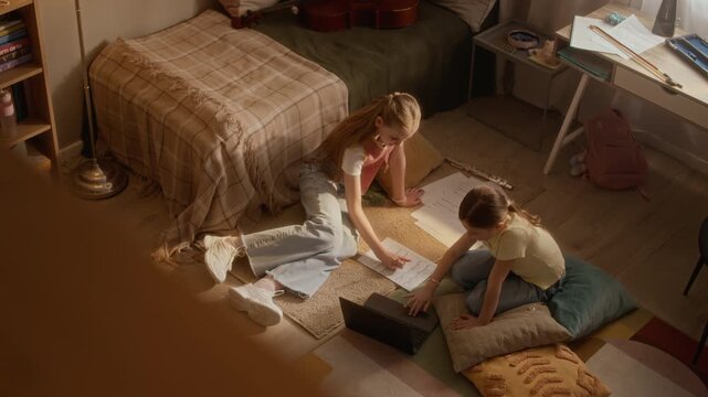 High angle of Caucasian teenager teaching music to younger child using laptop and sheet music on floor. Clip is perfect for promoting online tutoring services and e-learning platforms