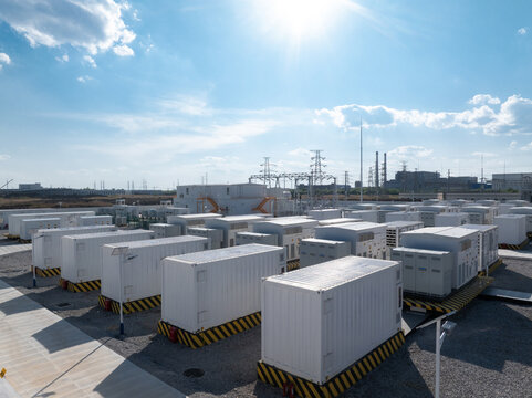 White containerized energy storage systems arranged in an outdoor power station facility