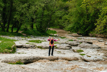 Obraz premium Happy woman with backpack looks up enjoying summer day by mountain river. Mindful travel and outdoor recreation