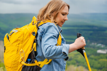 Profile portrait of mid adult woman in denim jacket with yellow backpack holding trekking pole. Nordic walking and active recreation concept. © 5ph