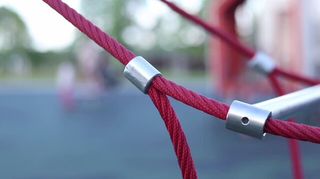 Rope fastening on a children's playground. Close-up of metal connectors of red reinforced ropes. Modern equipment for children's outdoor entertainment. Knot of fastening of rope structures