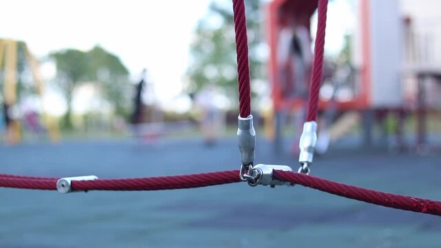 Rope fastening on a children's playground. Close-up of metal connectors of red reinforced ropes. Modern equipment for children's outdoor entertainment. Knot of fastening of rope structures
