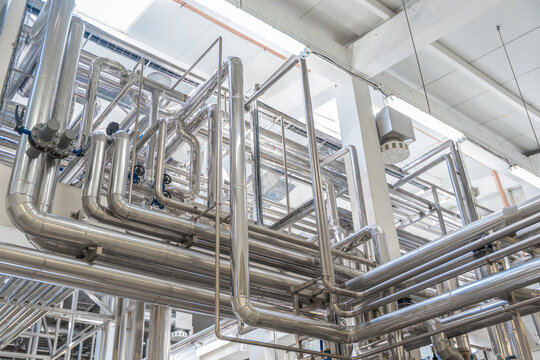 Modern industrial factory interior with stainless steel pipes and processing machinery. Clean automated production line in food, dairy, or chemical plant engineering industry.