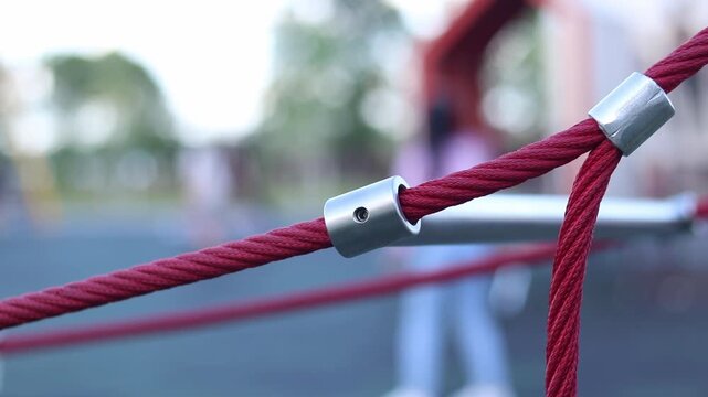 Rope fastening on a children's playground. Close-up of metal connectors of red reinforced ropes. Modern equipment for children's outdoor entertainment. Knot of fastening of rope structures