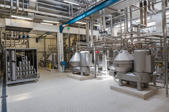 Modern industrial factory interior with stainless steel pipes and processing machinery. Clean automated production line in food, dairy, or chemical plant engineering industry.