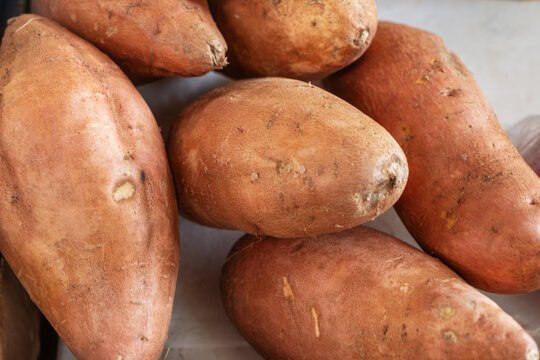 Fresh organic sweet potatoes stacked together on a light surface. Uncooked orange yams background for healthy food blogging and vegan recipe marketing